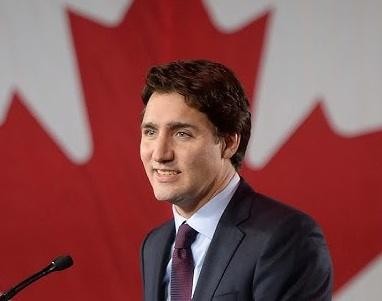 Justin Trudeau uśmiechnięty, w swobodnej interakcji z ludźmi, w tle rozmyty tłum.