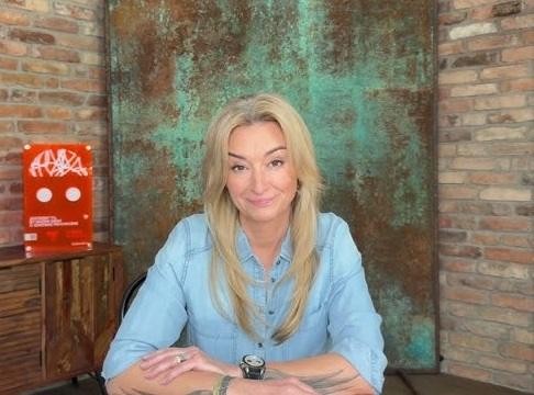 Martyna Wojciechowska w otoczeniu symbolizującym jej podróże i osiągnięcia, z elementami górskimi i mapą świata.