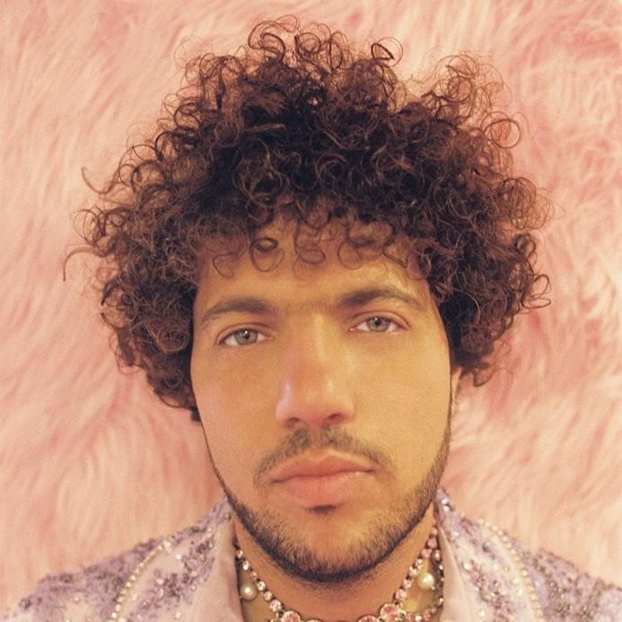 Benny Blanco pochylony nad konsolą mikserską, z zamyśloną miną, w otoczeniu sprzętu studyjnego, symbolizujący jego proces twórczy.
