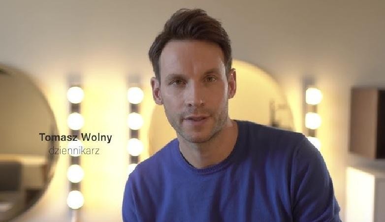 Tomasz Wolny podczas akcji charytatywnej, uśmiechnięty, w otoczeniu dzieci, symbolizujący jego zaangażowanie społeczne.