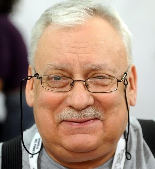 Skwer Geralta z Rivii w Łodzi, z widocznym pomnikiem lub tablicą pamiątkową, otoczony typową łódzką architekturą.