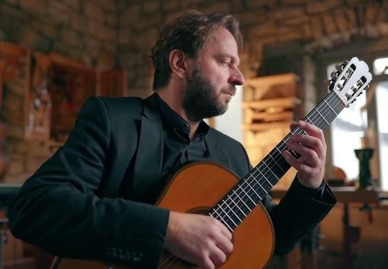 Marcin Dylla podczas dynamicznego występu na scenie, z rozmytymi dłońmi nad strunami gitary, oddający intensywność muzycznej ekspresji.