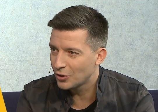 Michał Cessanis w swoim domu, siedzący w salonie, z elementami sugerującymi podróże i życie rodzinne w tle.