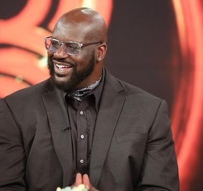 Shaquille O'Neal uśmiechnięty i zaangażowany w interakcję z fanami, ubrany w casualową odzież, prezentujący swoją charyzmatyczną osobowość.