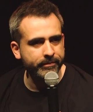 Abelard Giza na scenie podczas występu stand-upowego, trzymający mikrofon, z ekspresyjną mimiką.