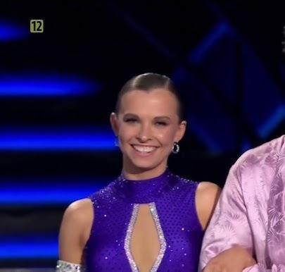 Ola Filipek w eleganckim stroju tanecznym, wykonująca figurę taneczną na parkiecie Tańca z Gwiazdami, z rozmytym tłem studia telewizyjnego.