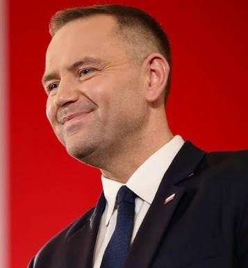 Karol Nawrocki przemawiający na tle historycznych symboli, podczas publicznego wystąpienia.