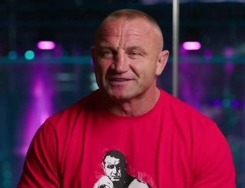 Alt: Mariusz Pudzianowski podczas intensywnego sparingu MMA w klatce, ukazujący dynamikę i siłę w walce.