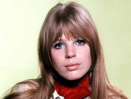 Marianne Faithfull na scenie w późnych latach 70., trzymająca mikrofon, z intensywnym wyrazem twarzy, w dynamicznym ujęciu.