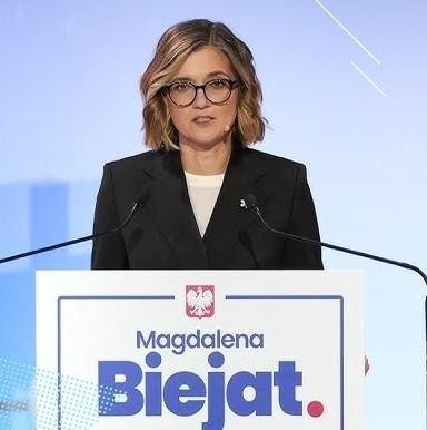 Magdalena Biejat podczas spotkania z wyborcami, uśmiechnięta i zaangażowana w rozmowę, na tle miejskiego krajobrazu.